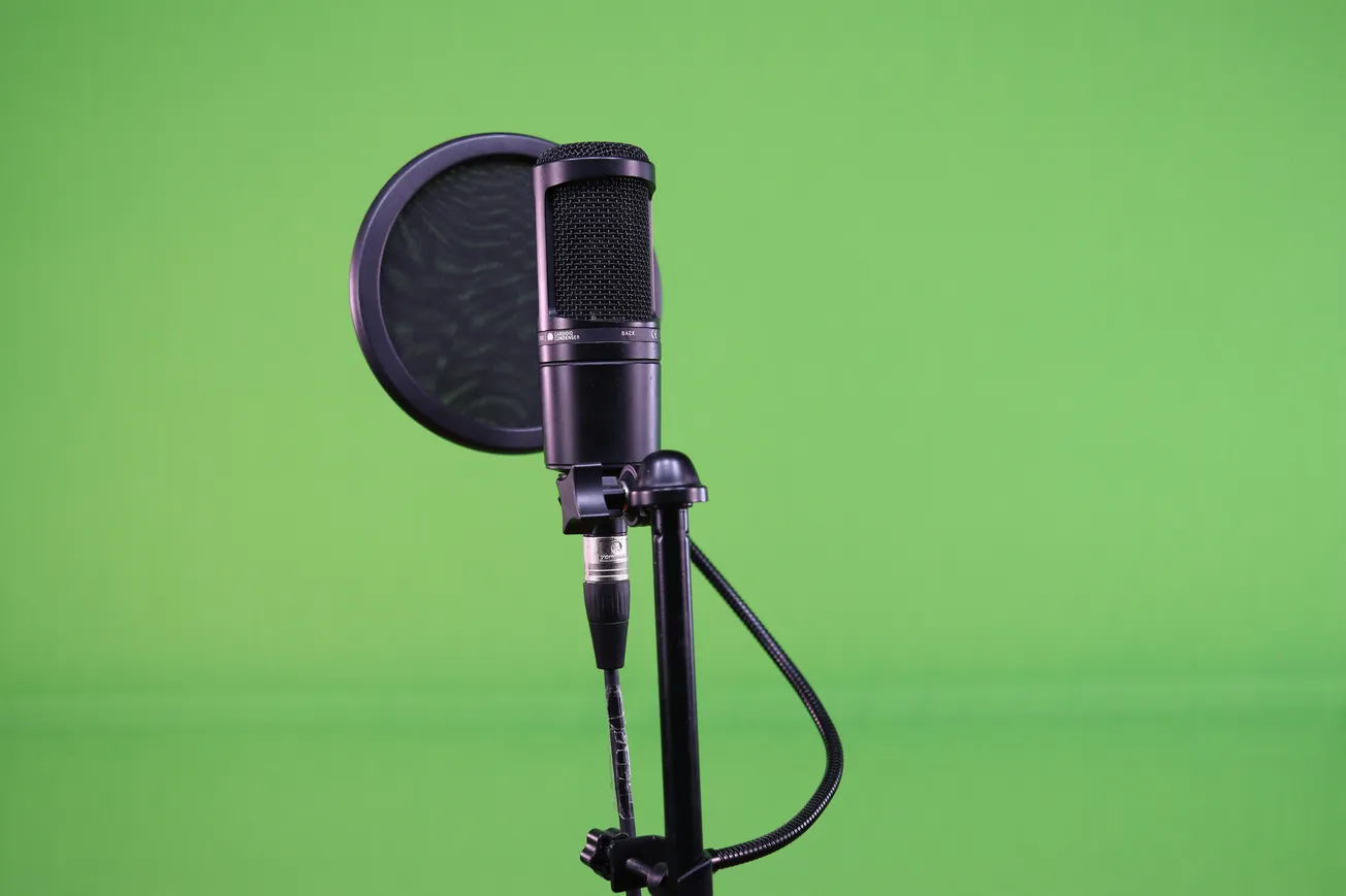 A black studio microphone with a pop filter on a stand is set against a vibrant green background, suggesting a professional recording setting.
