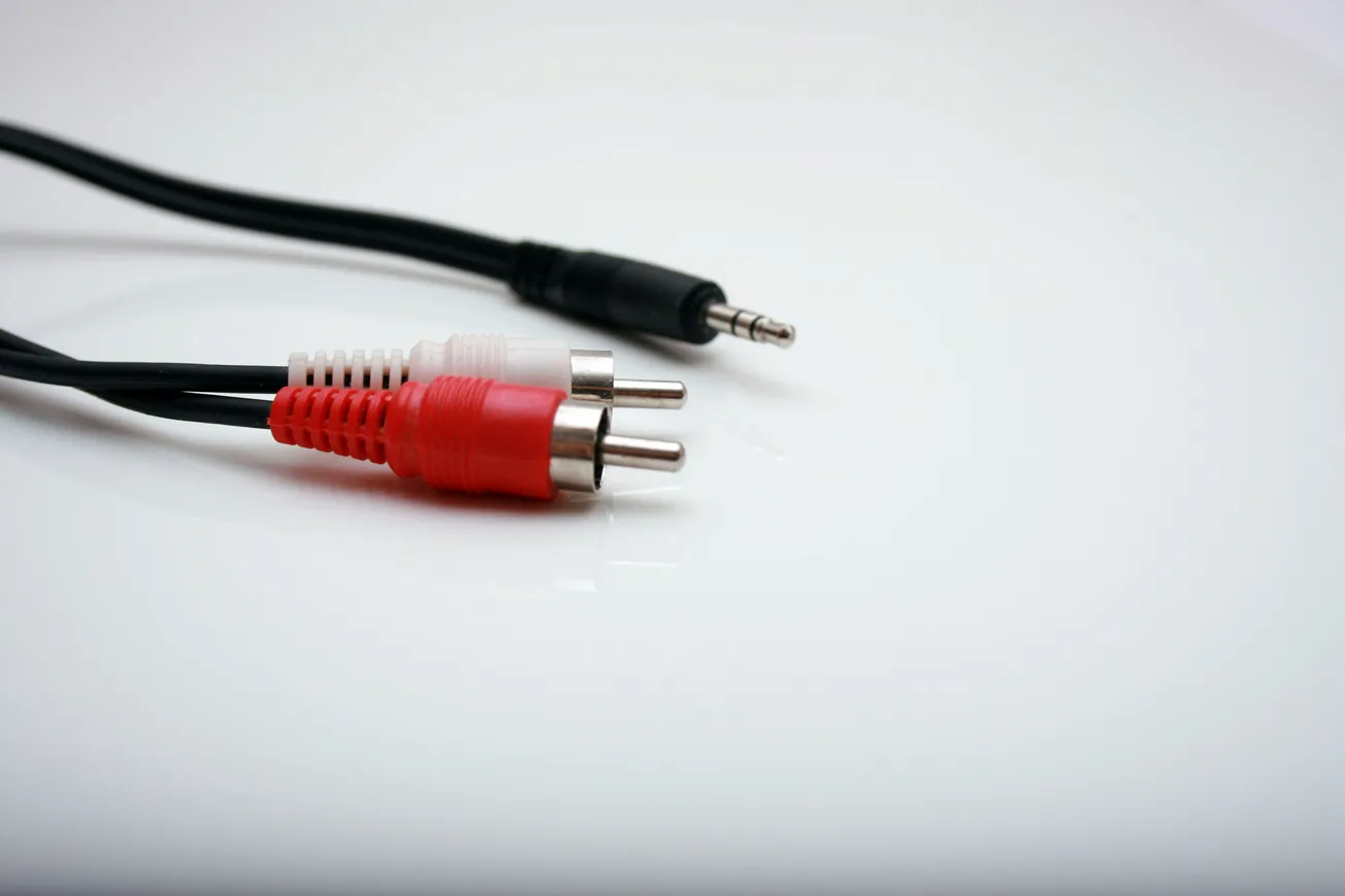 Close-up of a black audio cable with a 3.5mm jack, alongside a red and white RCA connector, on a white glossy surface.