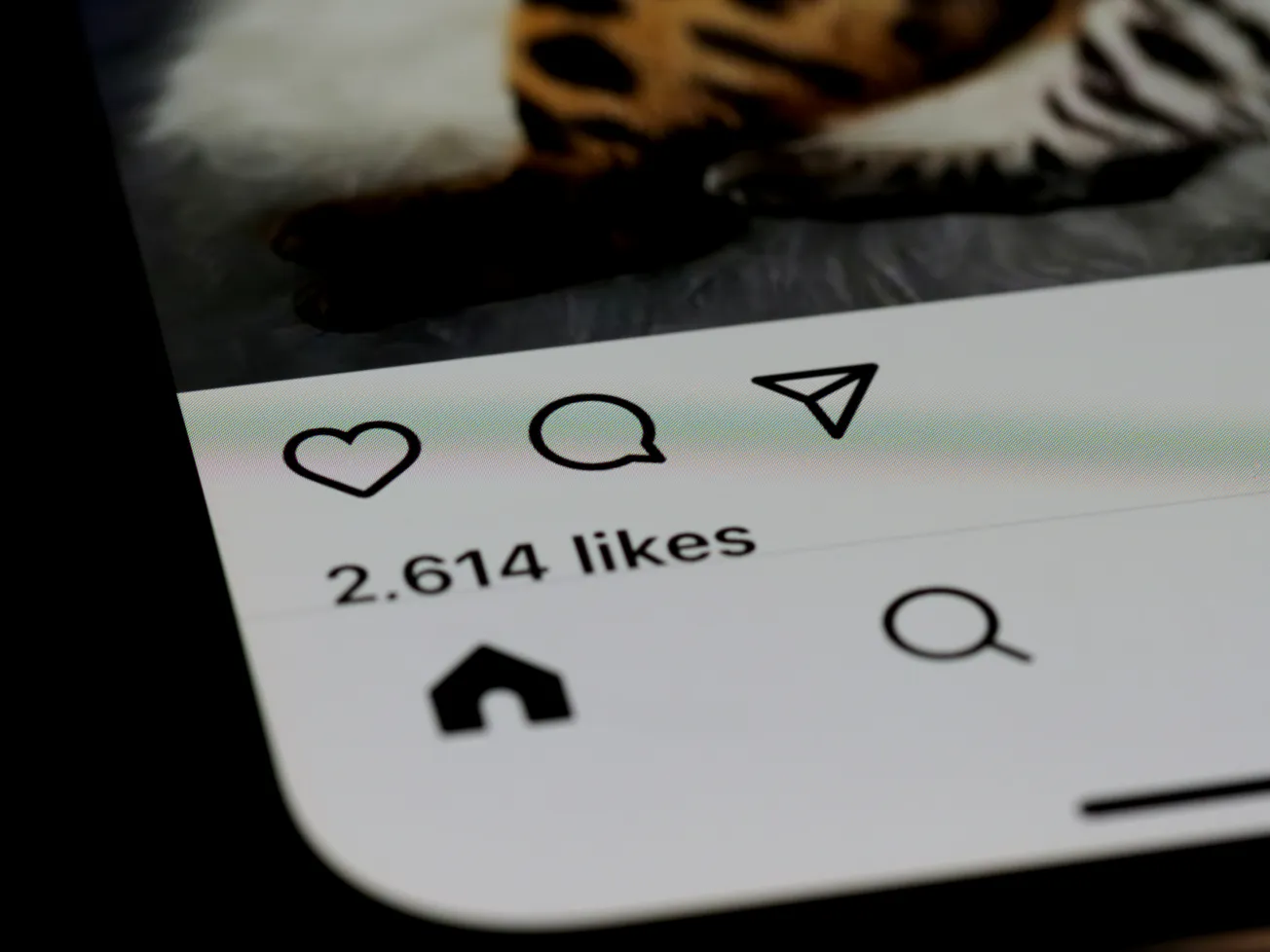 Close-up of a smartphone screen showing an Instagram post interface. It displays heart, chat, and share icons, with “2,614 likes” below.