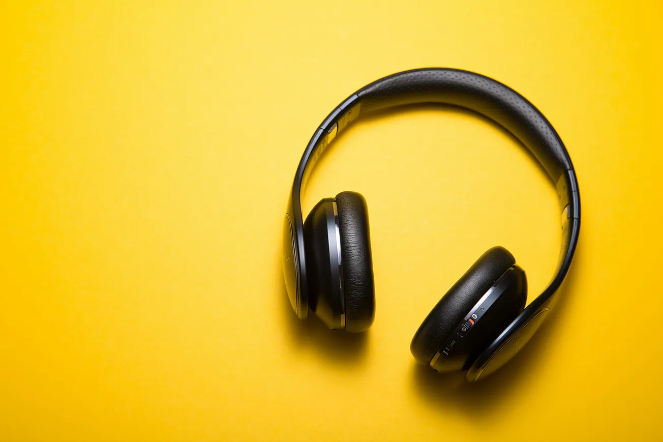 Black headphones with cushioned ear pads lie on a bright yellow background. The vibrant contrast creates a modern, energetic feel.
