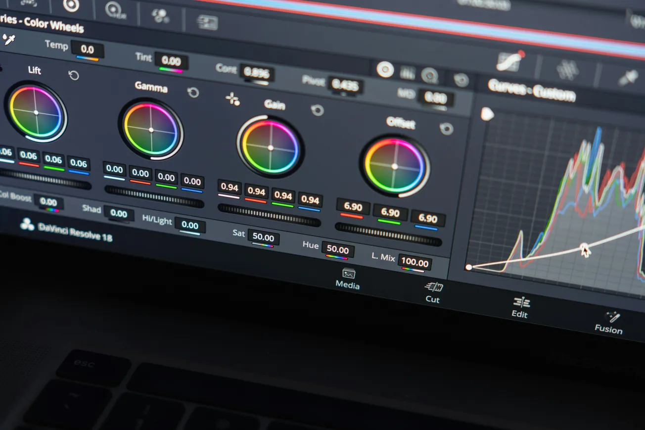 Close-up of a digital editing interface showing color wheels and a graph, indicating video color grading tools. The mood is technical and focused.