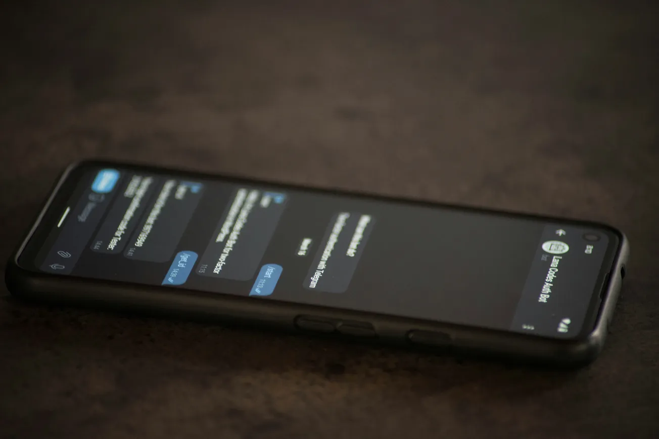 A smartphone displaying a dark-themed messaging app with multiple unread messages, lying on a dark surface. The atmosphere is casual and modern.
