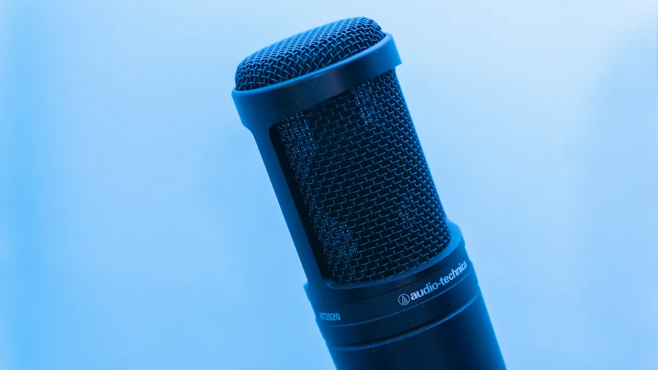 Close-up of a black microphone set against a light blue background. The image conveys a professional and cool ambiance, highlighting audio equipment.