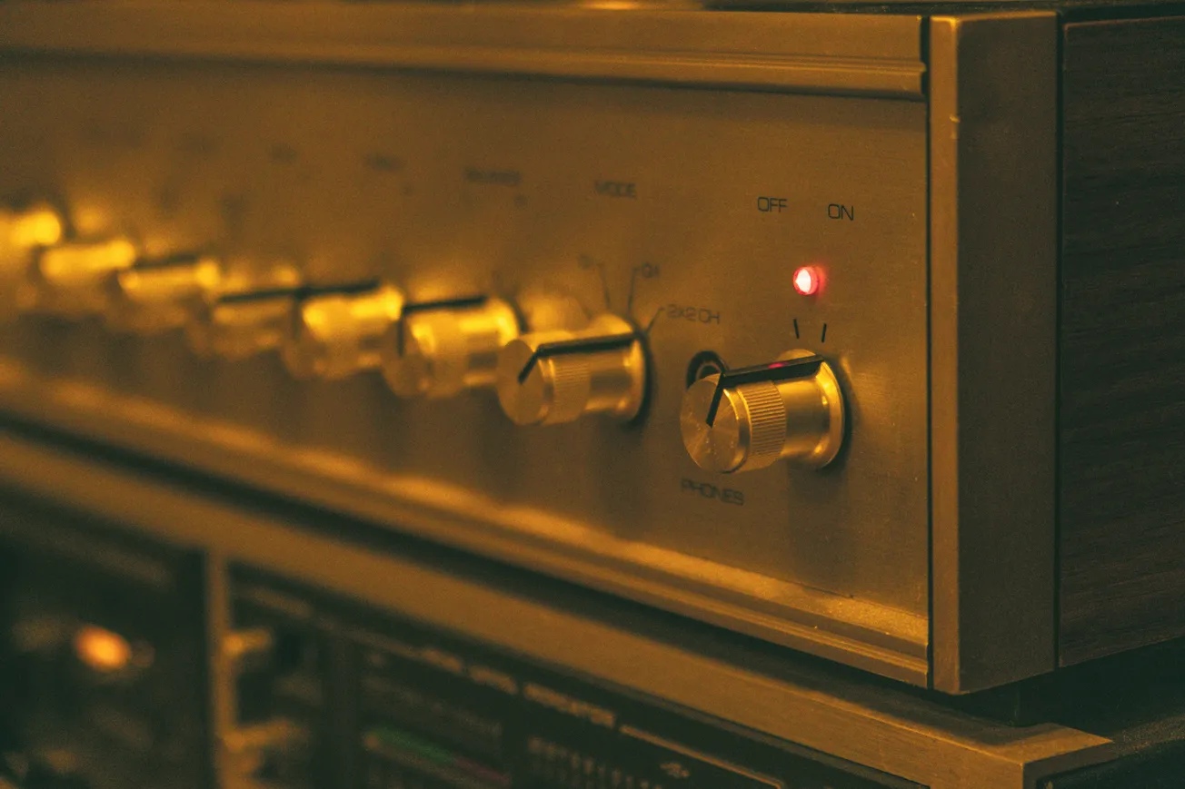 Close-up of a vintage audio receiver, featuring silver knobs and a glowing red power light, emits a nostalgic, warm, and retro ambiance.