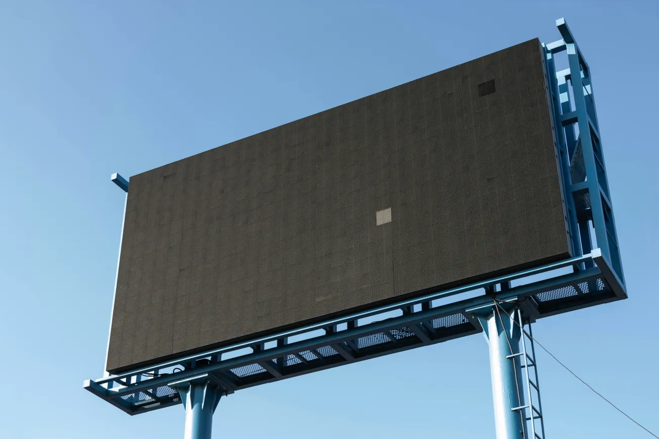 Large blank billboard on blue metal frame against clear blue sky. Captures a sense of emptiness and potential for advertising space.
