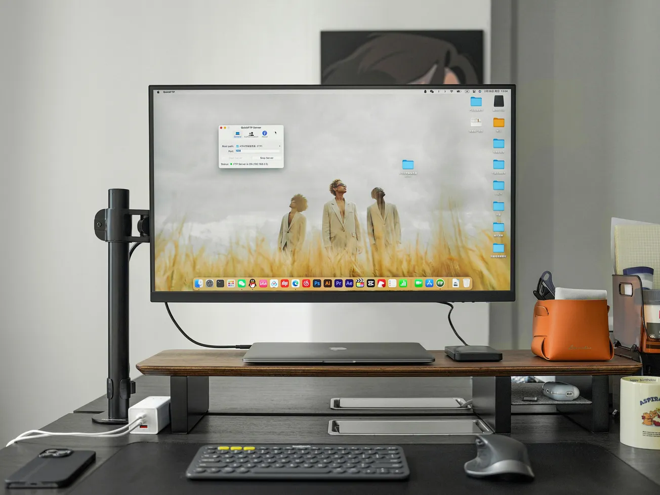 A modern workspace with a large monitor displaying three people in a field scene. The desk holds a sleek keyboard, mouse, and organized office supplies.