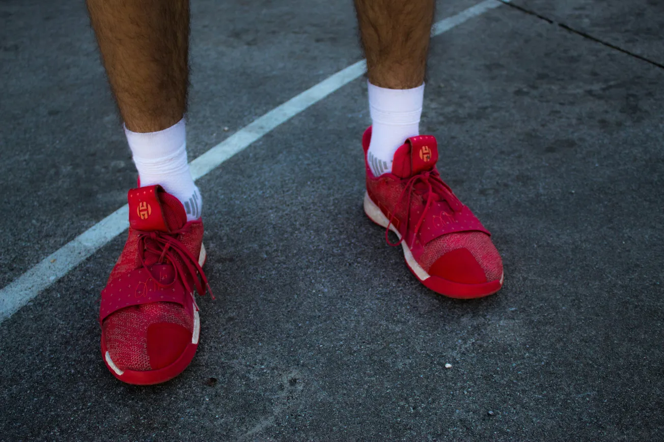 Close-up of a person wearing bright red athletic shoes and white socks standing on a concrete surface, showing part of a basketball court line.