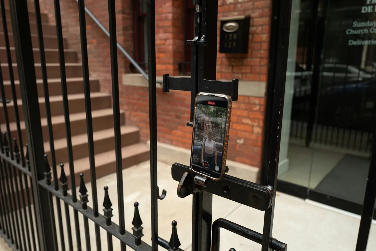 A cell phone is mounted on a metal gate as someone records a video of themselves from a distance.