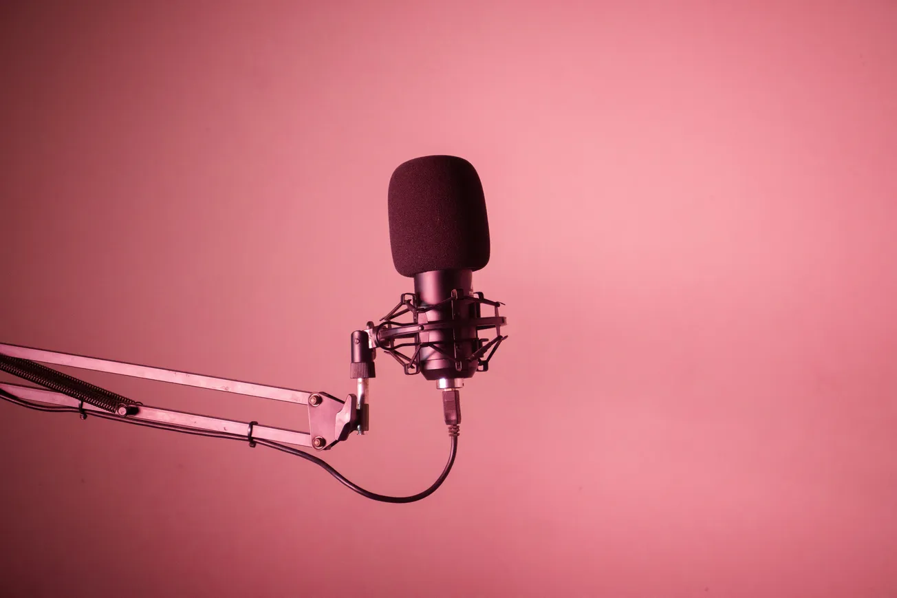A black microphone on a boom arm against a pink background. The setup suggests a podcast or recording studio, conveying a mood of creativity.