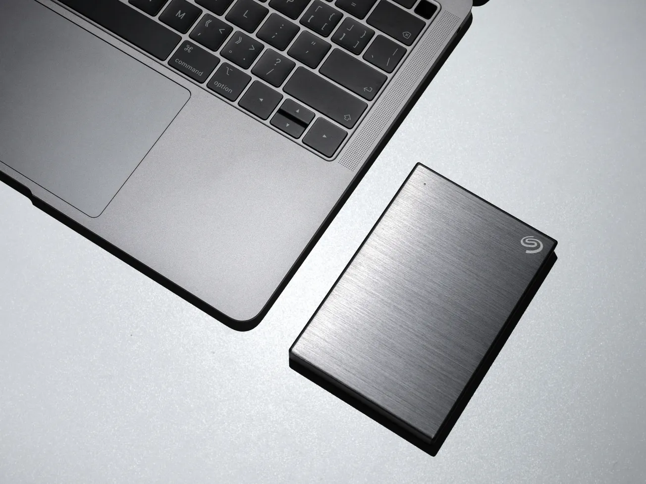 Laptop keyboard and sleek external hard drive placed on a reflective surface. The minimalist design conveys a modern, tech-savvy feel.