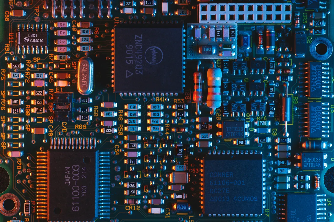 Close-up of a computer circuit board with various microchips and electronic components. It features a digital, intricate layout in blue and orange lighting.